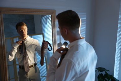 Photo of Man choosing neckties while getting ready near mirror indoors