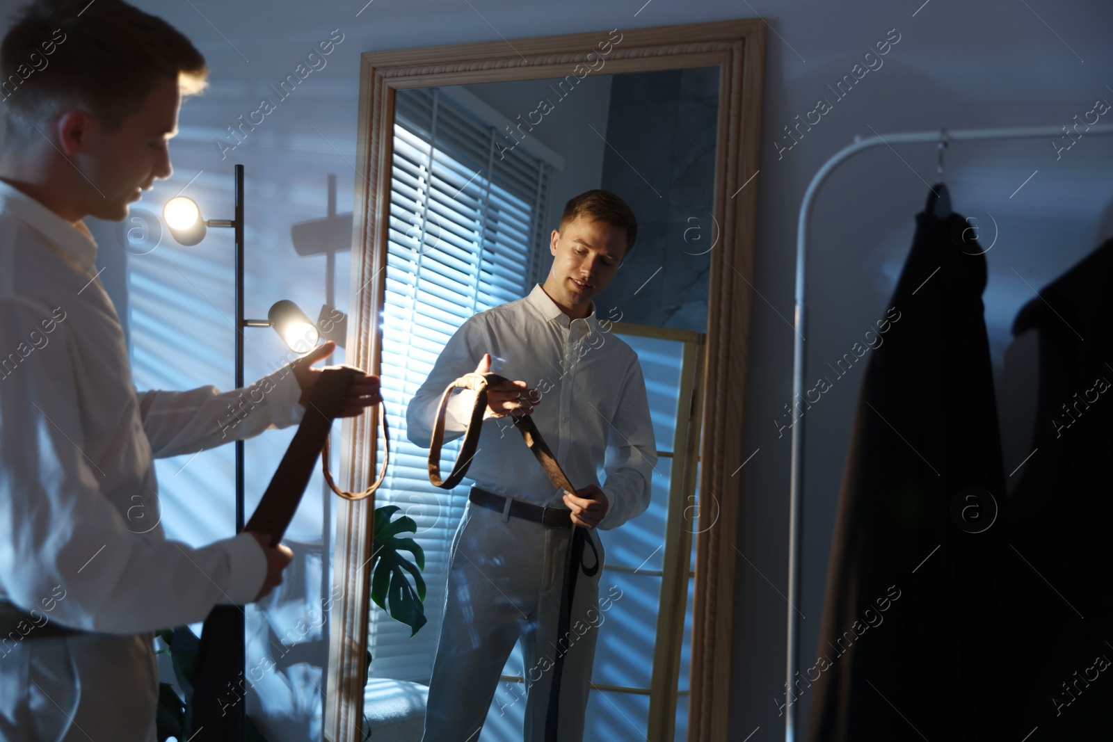 Photo of Man choosing neckties while getting ready near mirror indoors