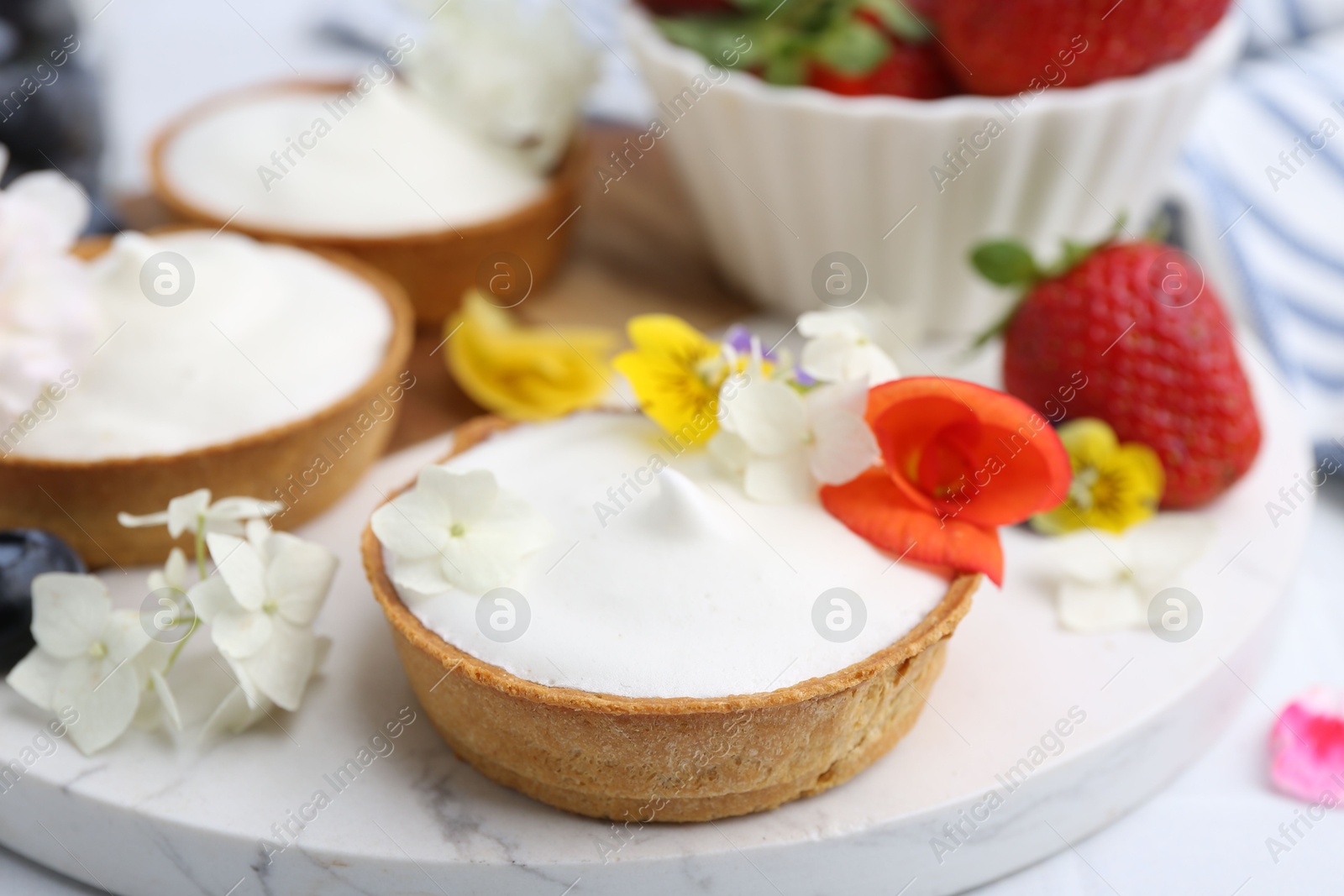 Delicious dessert. Tartlets with cream, berries and flowers on white tiled table, closeup Photo of Delicious dessert. Tartlets with cream, berries and flowers on white tiled table, closeup
