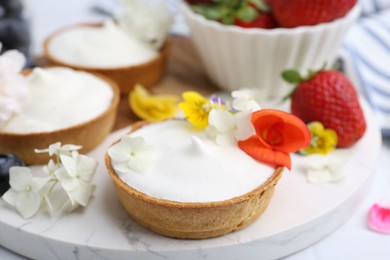 Photo of Delicious dessert. Tartlets with cream, berries and flowers on white tiled table, closeup