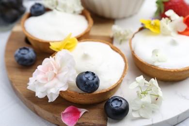 Photo of Delicious dessert. Tartlets with cream, berries and flowers on white tiled table, closeup