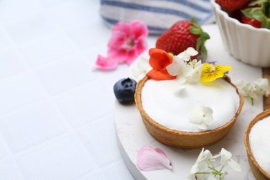 Photo of Delicious dessert. Tartlets with cream, berries and flowers on white tiled table, closeup. Space for text