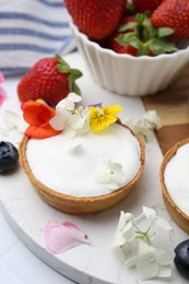 Photo of Delicious dessert. Tartlets with cream, berries and flowers on white tiled table, closeup