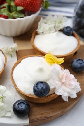 Photo of Delicious dessert. Tartlets with cream, berries and flowers on white tiled table, closeup