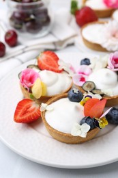 Photo of Delicious dessert. Tartlets with cream, berries and flowers on white tiled table, closeup