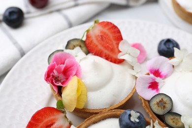 Photo of Delicious dessert. Tartlets with cream, berries and flowers on white tiled table, closeup
