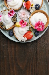 Photo of Delicious dessert. Tartlets with cream, berries and flowers on wooden table, top view. Space for text