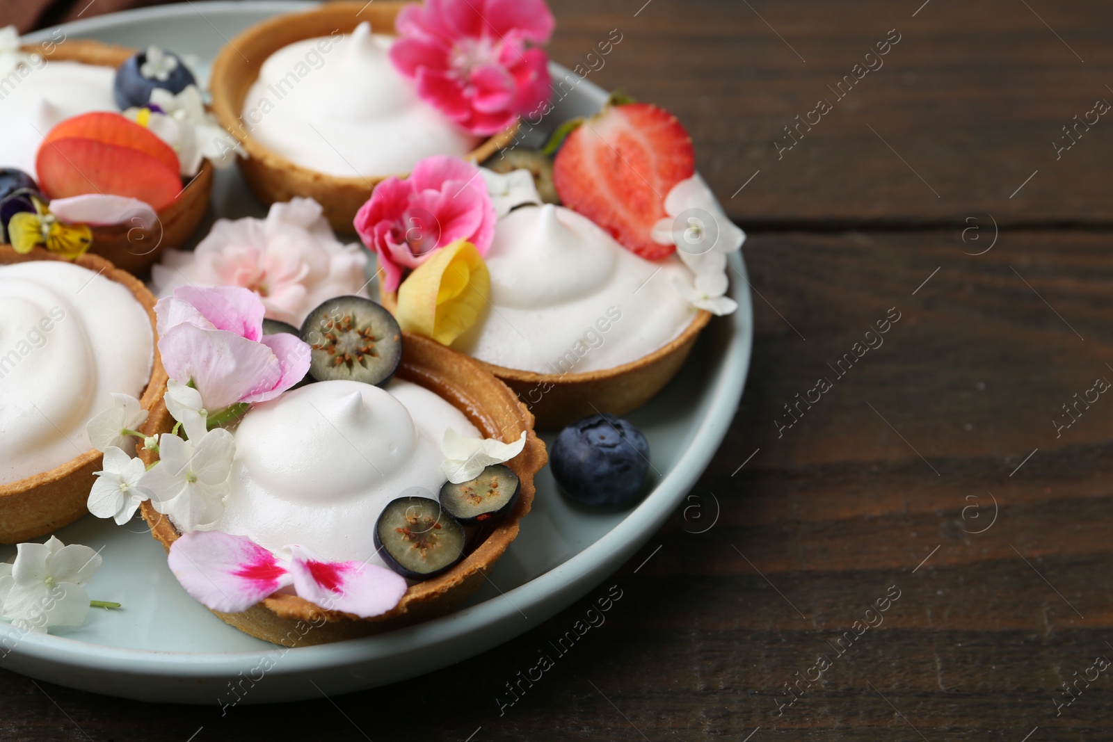 Delicious dessert. Tartlets with cream, berries and flowers on wooden table, closeup. Space for text Photo of Delicious dessert. Tartlets with cream, berries and flowers on wooden table, closeup. Space for text