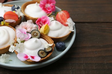 Photo of Delicious dessert. Tartlets with cream, berries and flowers on wooden table, closeup. Space for text