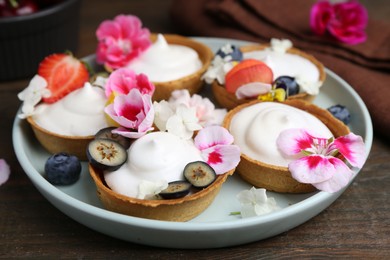 Photo of Delicious dessert. Tartlets with cream, berries and flowers on wooden table, closeup