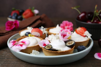 Photo of Delicious dessert. Tartlets with cream, berries and flowers on wooden table, closeup