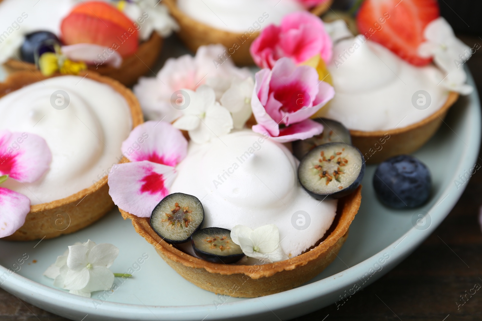 Delicious dessert. Tartlets with cream, berries and flowers on wooden table, closeup Photo of Delicious dessert. Tartlets with cream, berries and flowers on wooden table, closeup