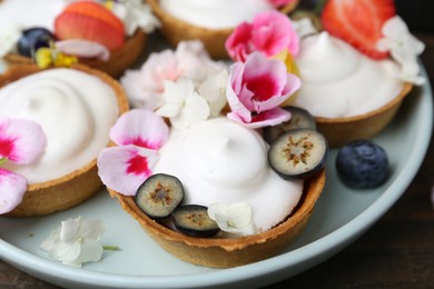 Photo of Delicious dessert. Tartlets with cream, berries and flowers on wooden table, closeup
