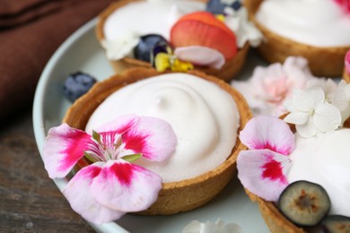 Photo of Delicious dessert. Tartlets with cream, berries and flowers on wooden table, closeup