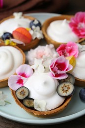 Photo of Delicious dessert. Tartlets with cream, berries and flowers on wooden table, closeup