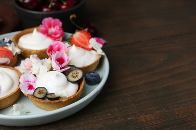 Photo of Delicious dessert. Tartlets with cream, berries and flowers on wooden table, closeup. Space for text
