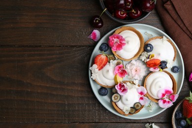 Photo of Delicious dessert. Tartlets with cream, berries and flowers on wooden table, flat lay