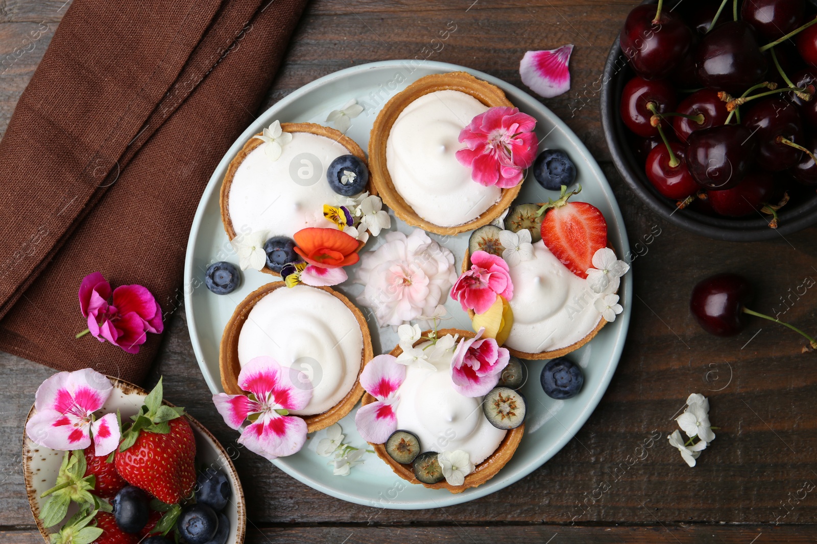Delicious dessert. Tartlets with cream, berries and flowers on wooden table, flat lay Photo of Delicious dessert. Tartlets with cream, berries and flowers on wooden table, flat lay