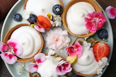 Photo of Delicious dessert. Tartlets with cream, berries and flowers on wooden table, flat lay