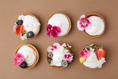 Photo of Delicious dessert. Tartlets with cream, berries and flowers on light brown background, flat lay