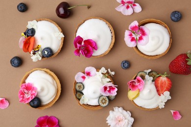 Photo of Delicious dessert. Tartlets with cream, berries and flowers on light brown background, flat lay