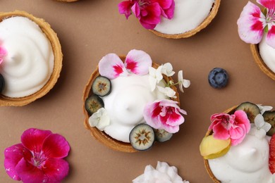 Photo of Delicious dessert. Tartlets with cream, berries and flowers on light brown background, flat lay