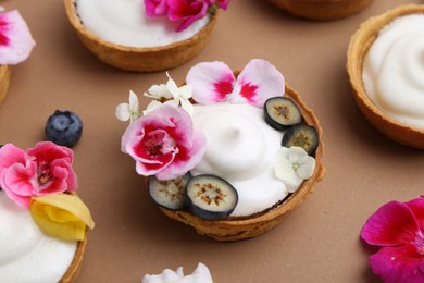 Photo of Delicious dessert. Tartlets with cream, berries and flowers on light brown background, closeup