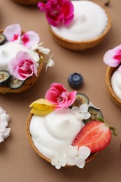 Photo of Delicious dessert. Tartlets with cream, berries and flowers on light brown background, closeup