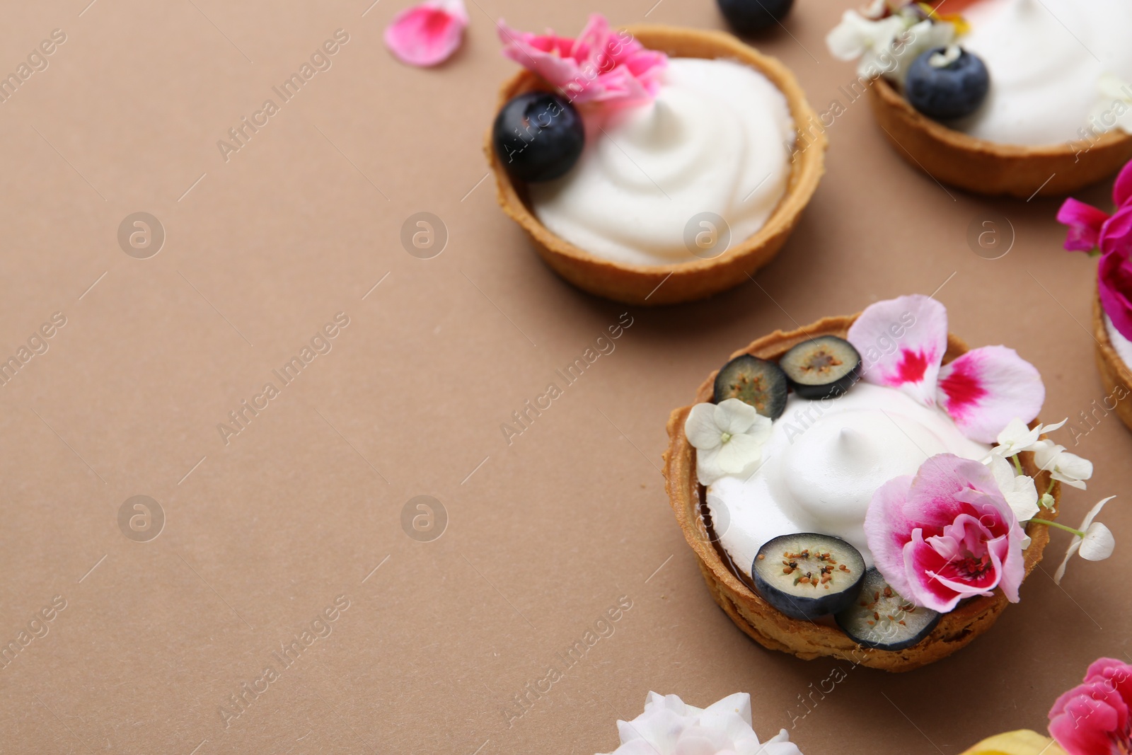 Delicious dessert. Tartlets with cream, berries and flowers on light brown background, closeup. Space for text Photo of Delicious dessert. Tartlets with cream, berries and flowers on light brown background, closeup. Space for text