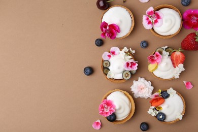 Photo of Delicious dessert. Tartlets with cream, berries and flowers on light brown background, flat lay. Space for text