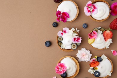 Photo of Delicious dessert. Tartlets with cream, berries and flowers on light brown background, flat lay. Space for text