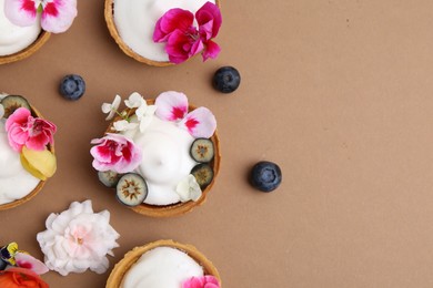 Photo of Delicious dessert. Tartlets with cream, berries and flowers on light brown background, flat lay. Space for text