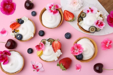 Photo of Delicious dessert. Tartlets with cream, berries and flowers on pink background, flat lay