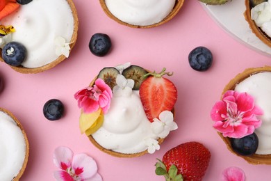 Photo of Delicious dessert. Tartlets with cream, berries and flowers on pink background, flat lay