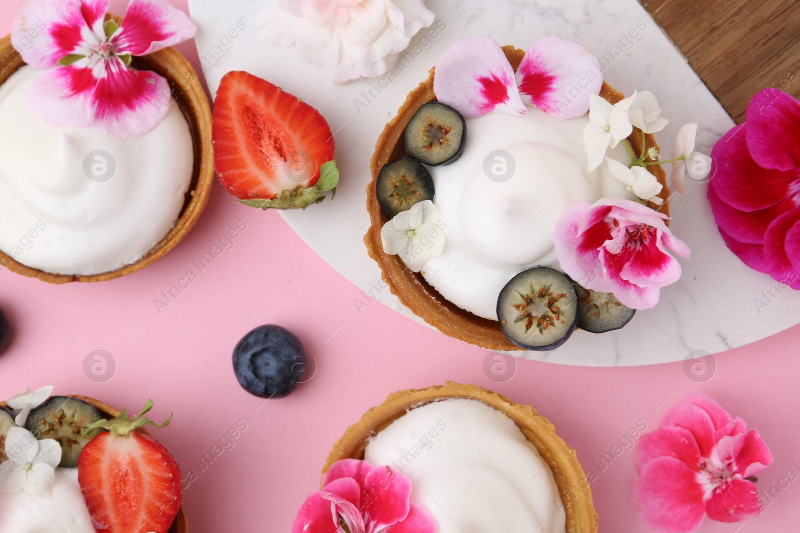 Delicious dessert. Tartlets with cream, berries and flowers on pink background, flat lay Photo of Delicious dessert. Tartlets with cream, berries and flowers on pink background, flat lay