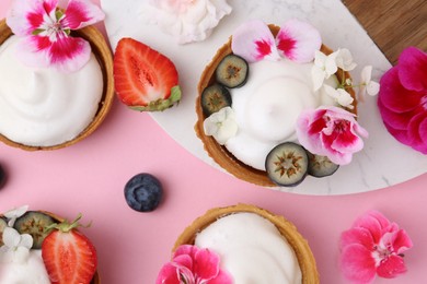 Photo of Delicious dessert. Tartlets with cream, berries and flowers on pink background, flat lay