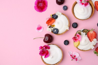 Photo of Delicious dessert. Tartlets with cream, berries and flowers on pink background, flat lay. Space for text