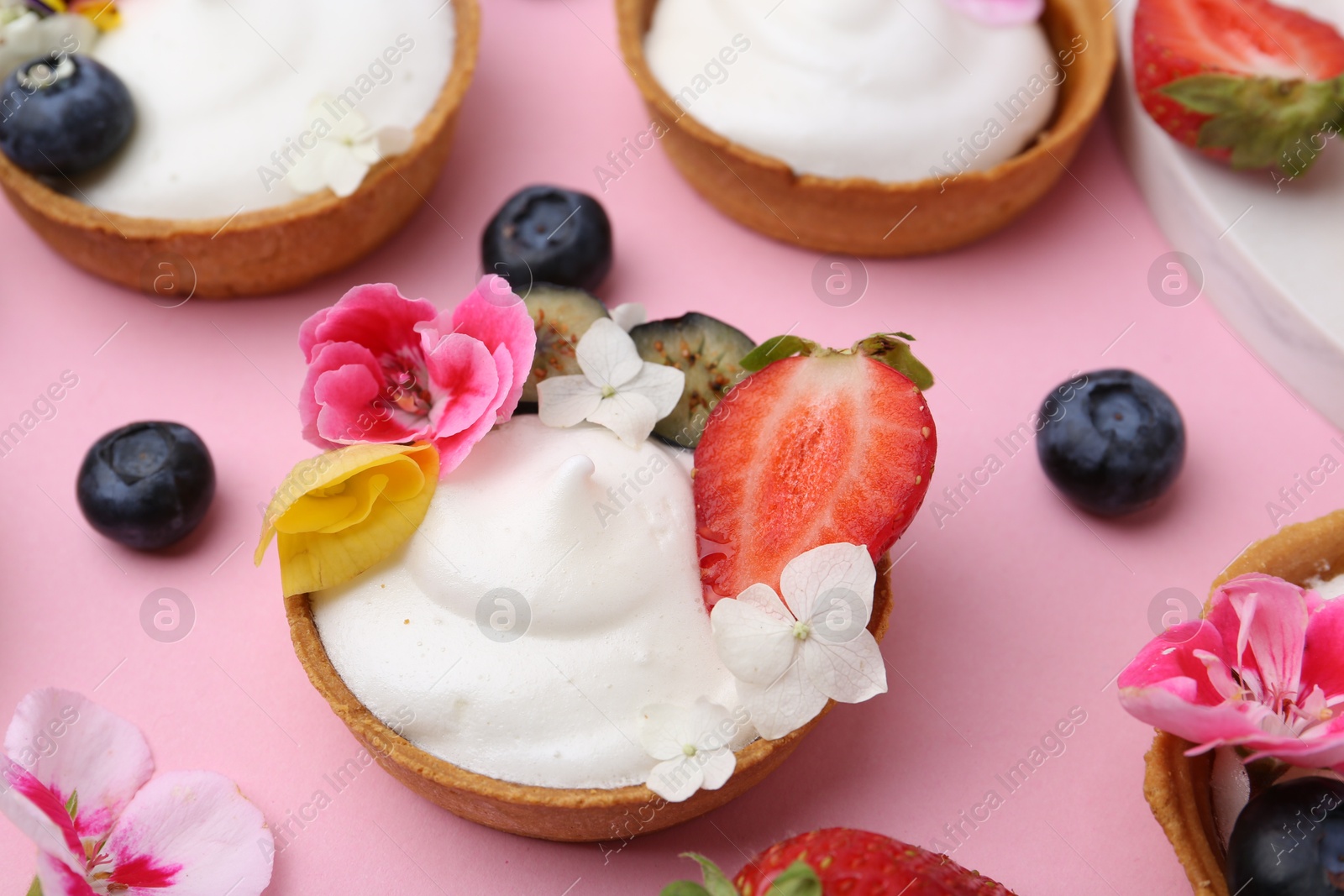 Photo of Delicious dessert. Tartlets with cream, berries and flowers on pink background, closeup