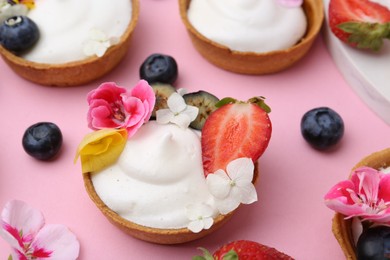 Photo of Delicious dessert. Tartlets with cream, berries and flowers on pink background, closeup