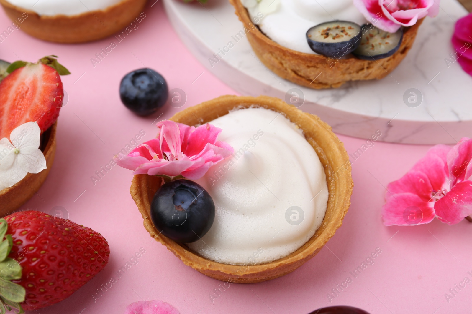 Delicious dessert. Tartlets with cream, berries and flowers on pink background, closeup Photo of Delicious dessert. Tartlets with cream, berries and flowers on pink background, closeup