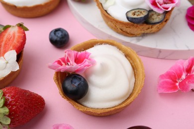 Photo of Delicious dessert. Tartlets with cream, berries and flowers on pink background, closeup