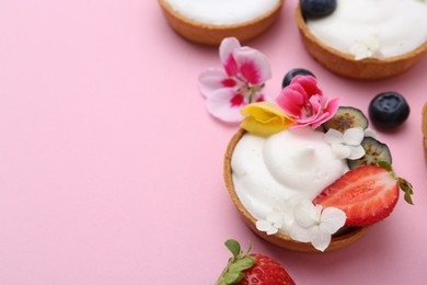 Photo of Delicious dessert. Tartlets with cream, berries and flowers on pink background, closeup. Space for text