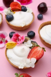 Photo of Delicious dessert. Tartlets with cream, berries and flowers on pink background, closeup