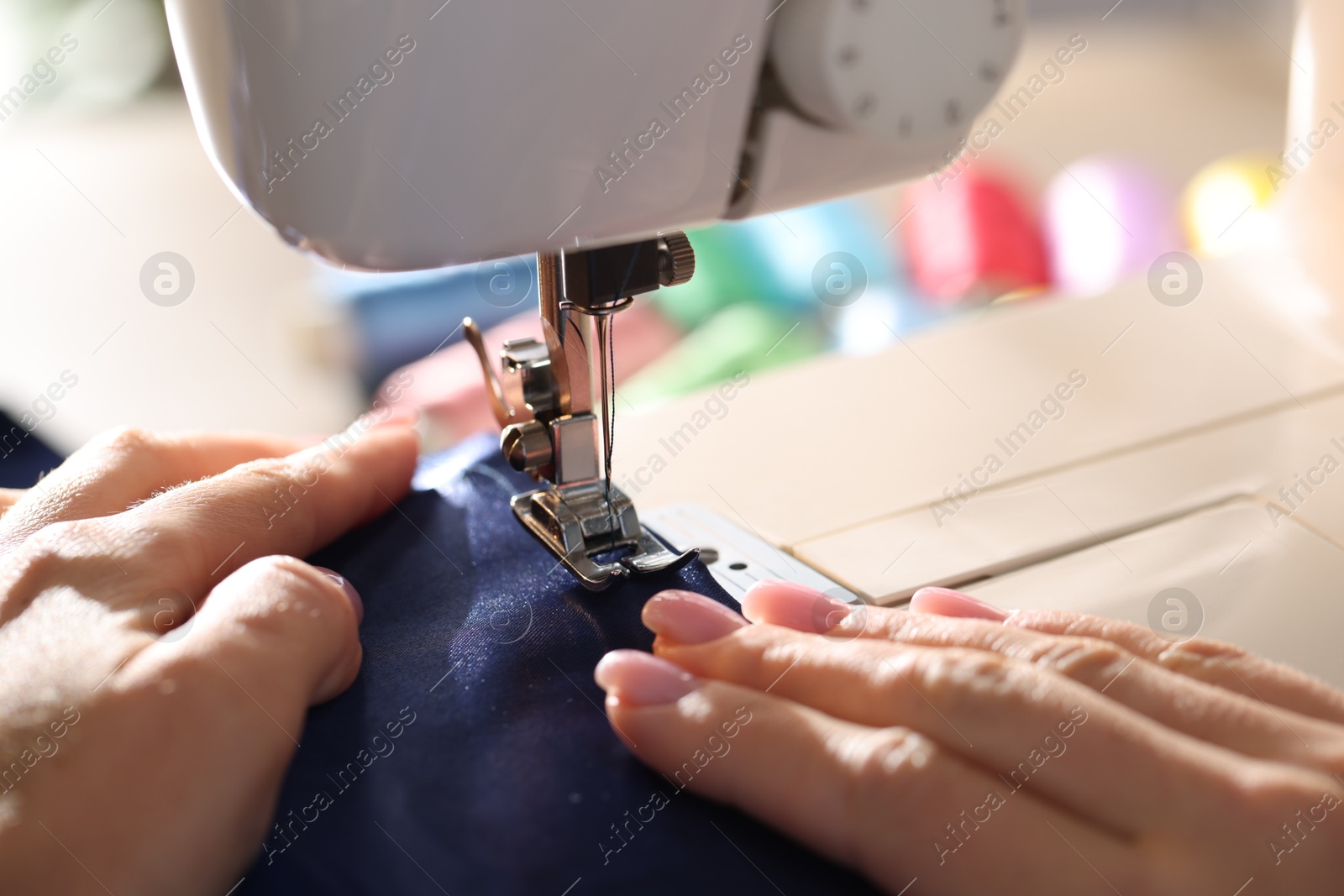 Woman working with sewing machine on blurred background, macro view Photo of Woman working with sewing machine on blurred background, macro view
