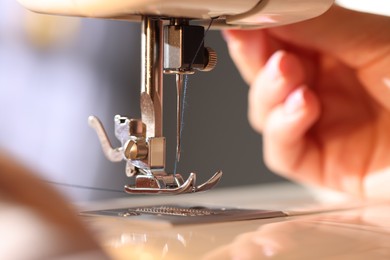Photo of Woman threading sewing machine needle on blurred grey background, macro view