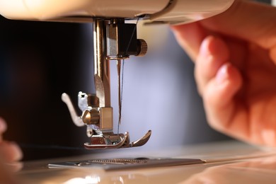Photo of Woman threading sewing machine needle on blurred grey background, macro view