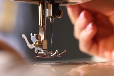 Photo of Woman threading sewing machine needle on blurred grey background, macro view