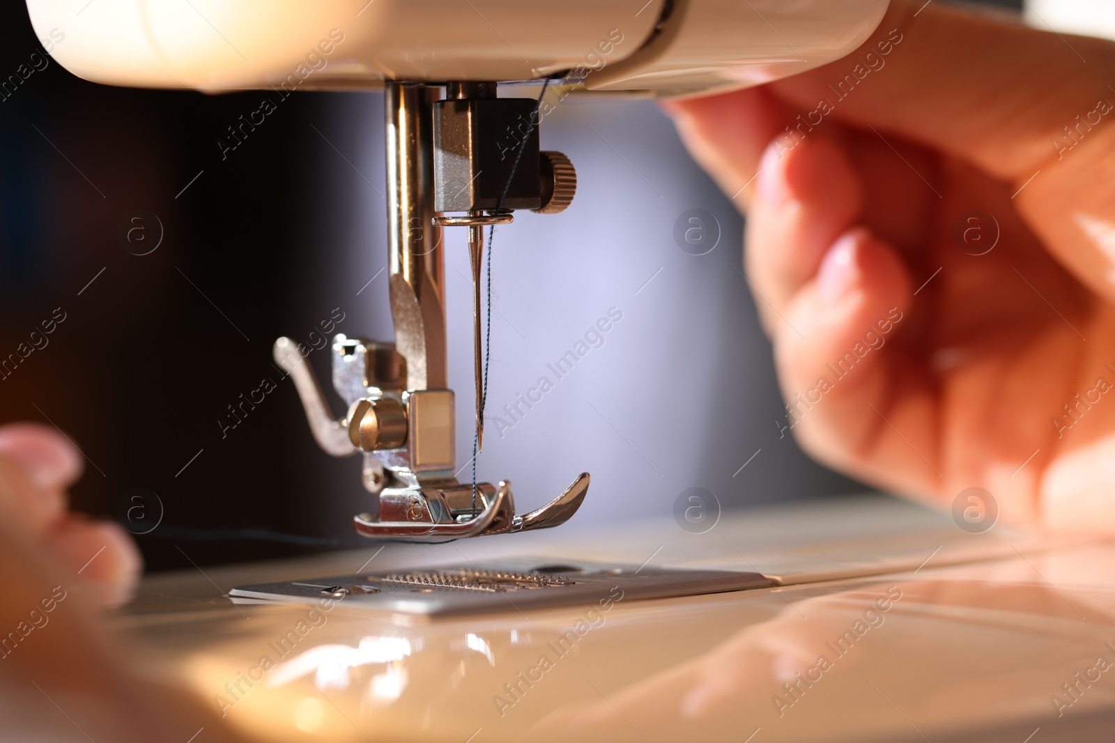 Woman threading sewing machine needle on blurred grey background, macro view Photo of Woman threading sewing machine needle on blurred grey background, macro view