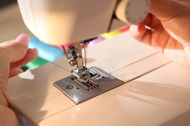 Photo of Woman threading sewing machine needle on blurred background, macro view