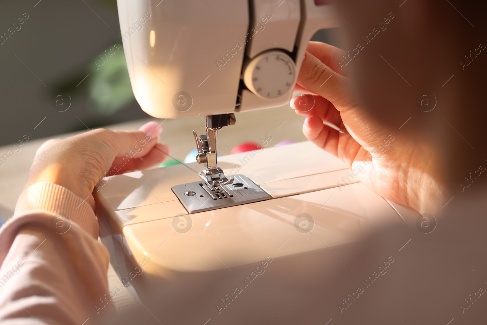 Photo of Woman threading sewing machine needle on blurred background, macro view